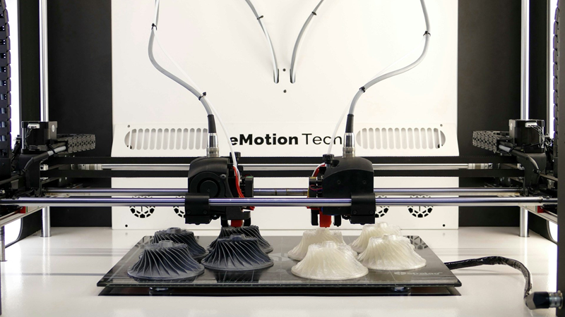 A dual-extruder 3D printer printing black and white parts at the same time.